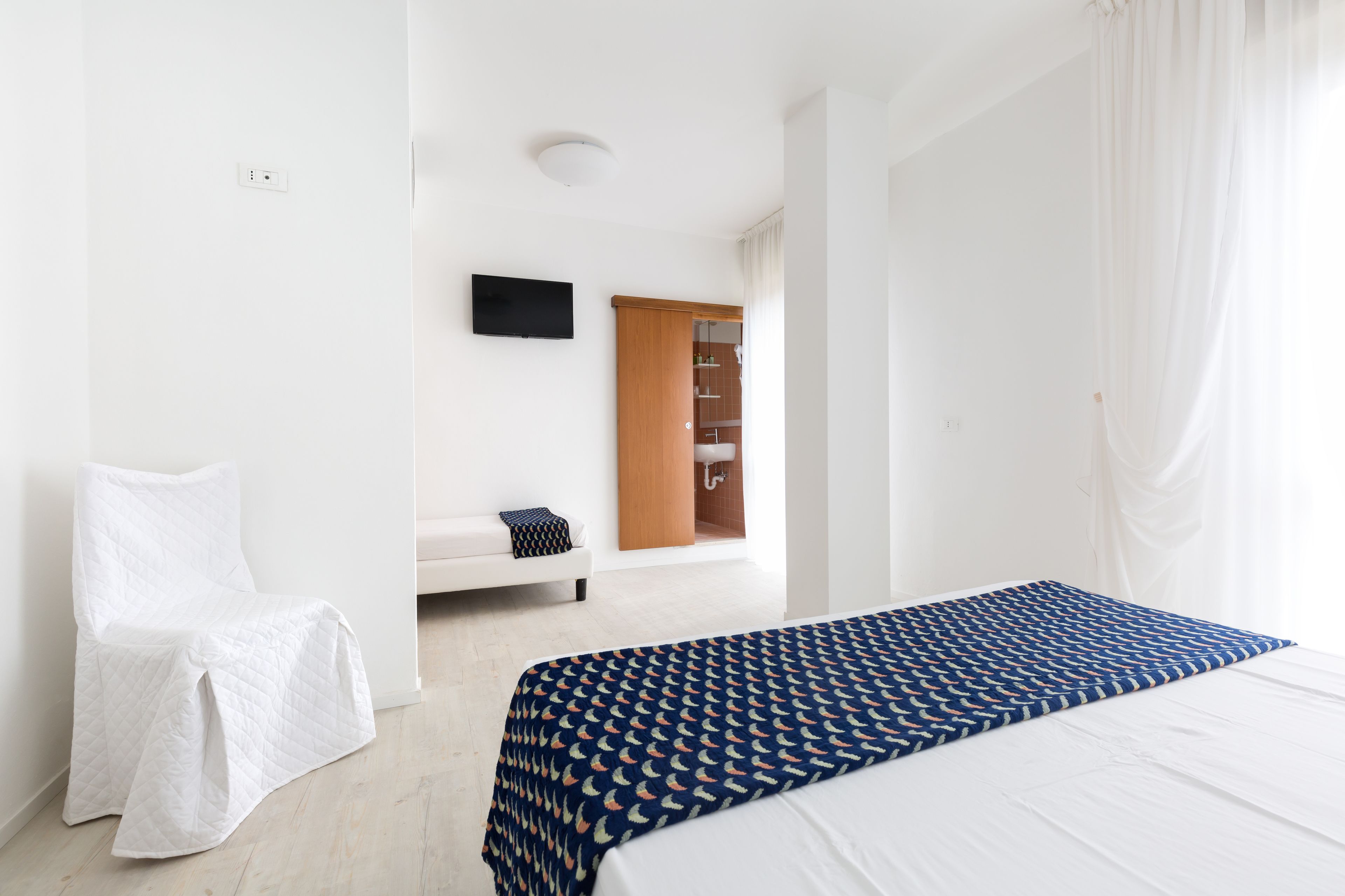 A bedroom with a bed, a chair, a TV, and a wardrobe.