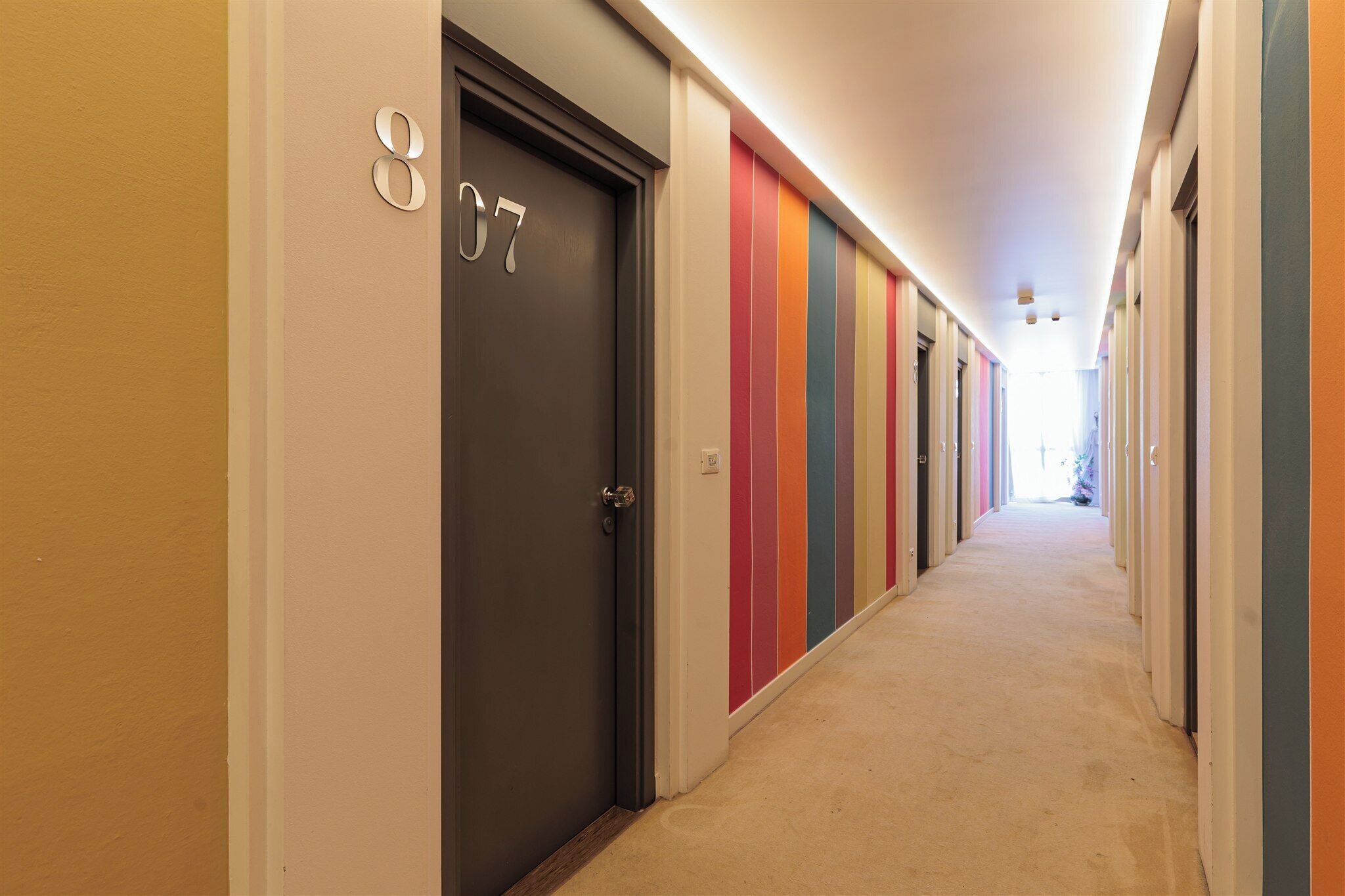 Pasillo de hotel con puertas numeradas 807 y 808, piso alfombrado y techo de color claro.