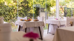A dining area with tables set for breakfast, surrounded by large windows offering a view of greenery.