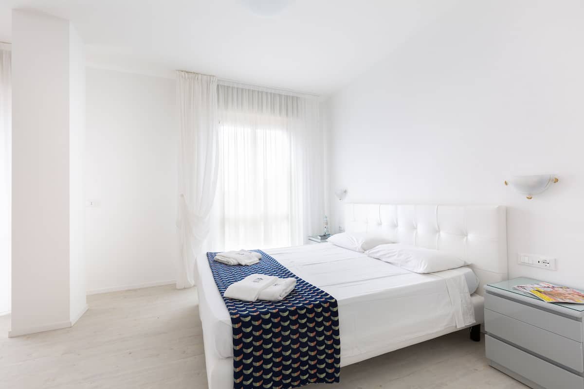 A neatly arranged bedroom with a bed, a bedside table, and a window with curtains.