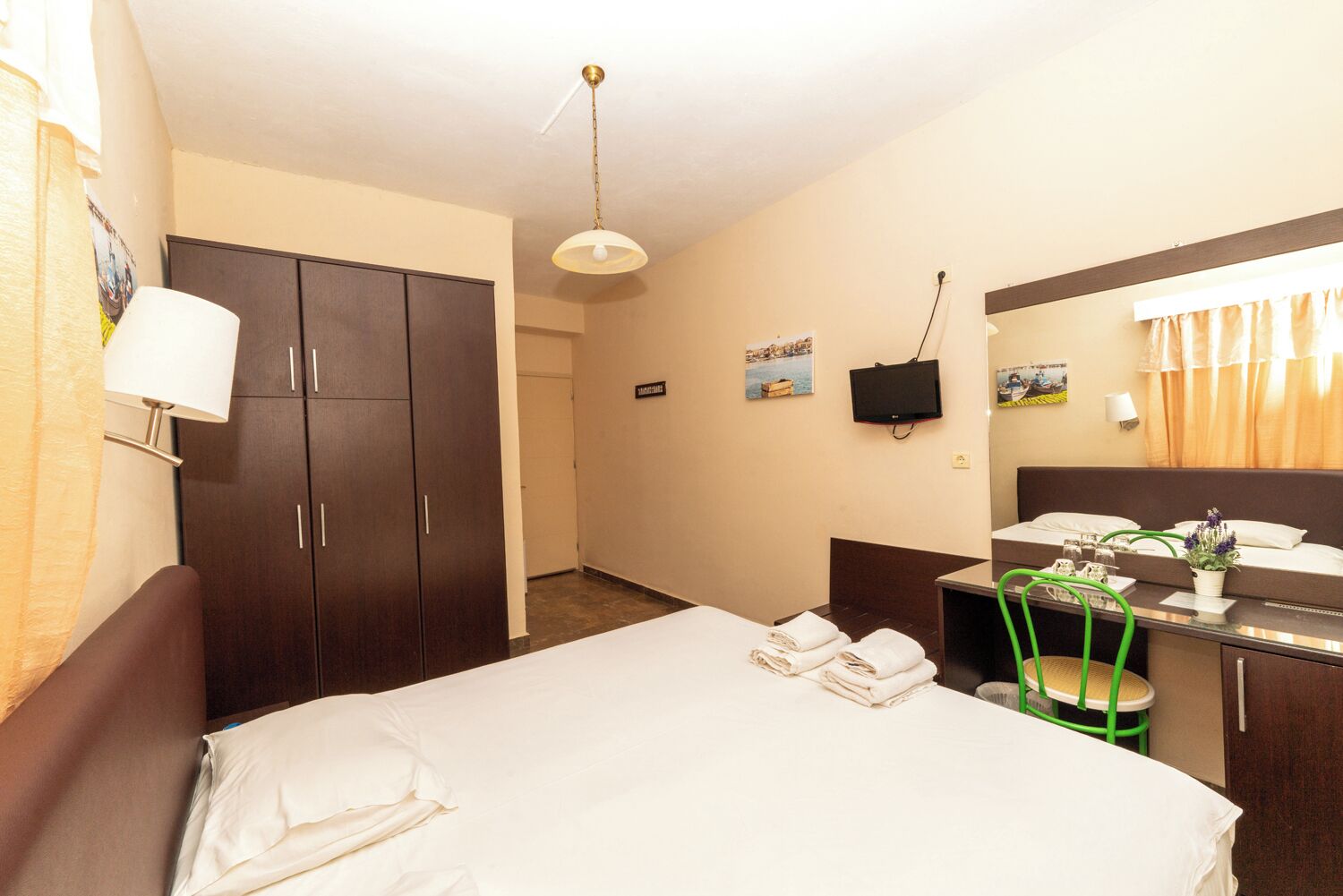 Habitación de hotel con cama, escritorio, silla, armario, televisión y baño.