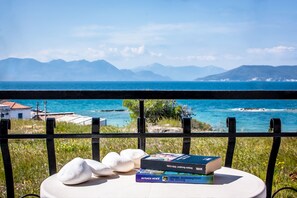 Vista del mar con montañas al fondo, una barandilla y una mesa con libros y piedras.