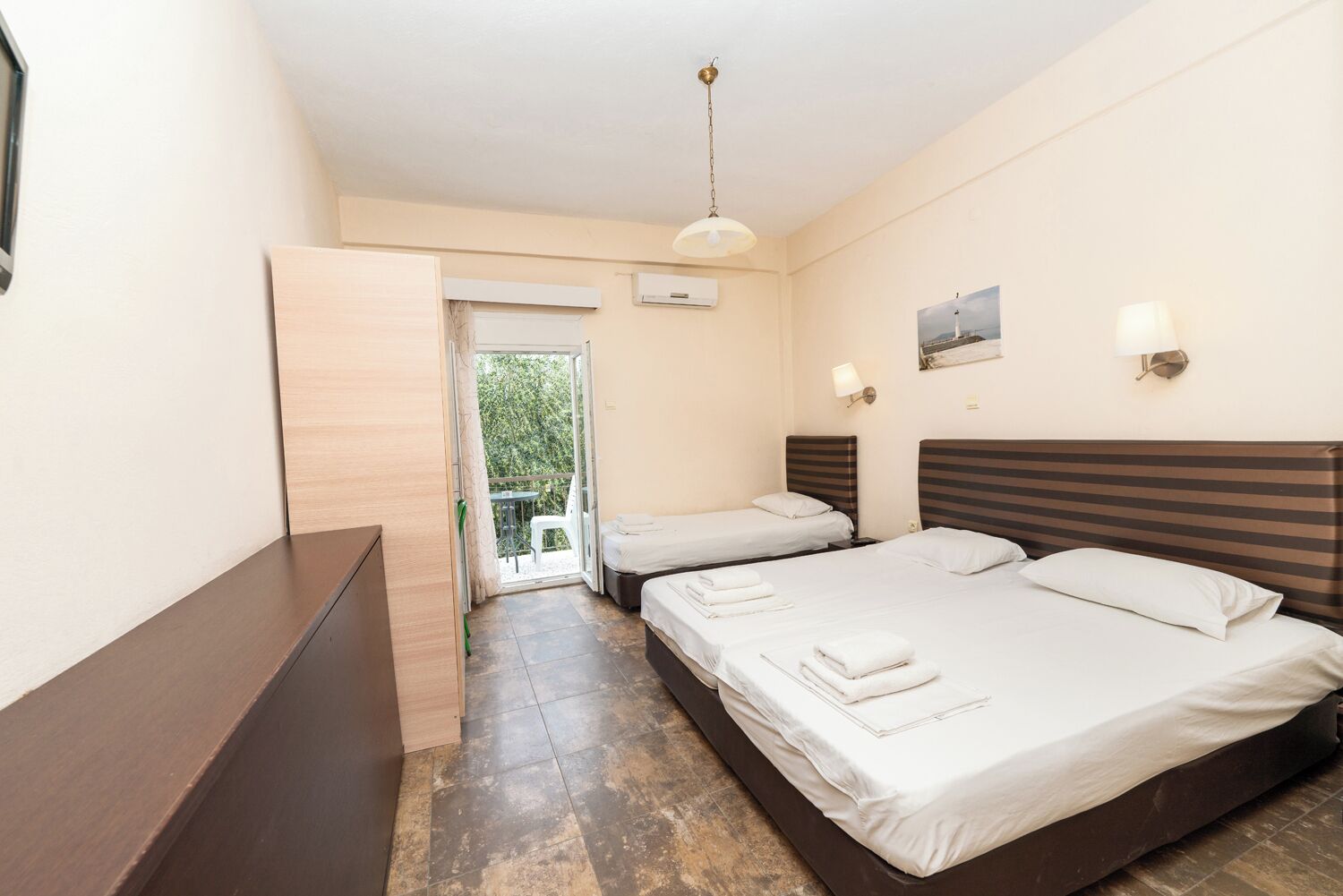 Habitación de hotel con dos camas, un escritorio de madera, un balcón y una lámpara en el techo.