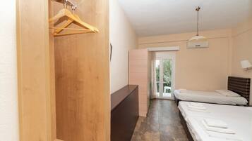 A hotel room with a wooden wardrobe, a desk, two beds, and a view of the outdoors through a glass door.