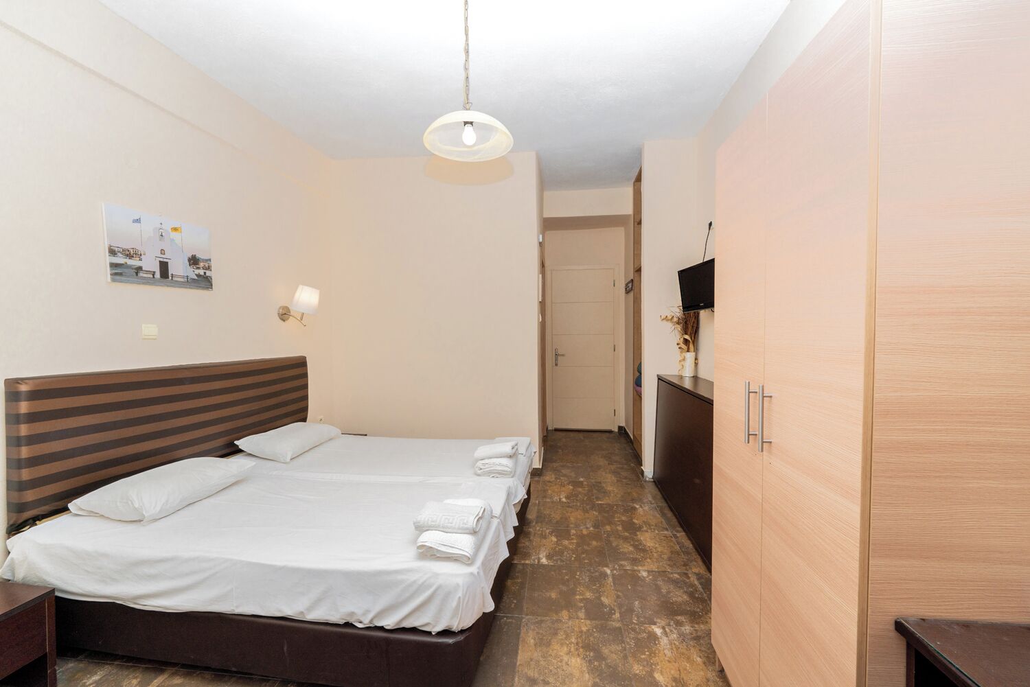 A hotel room with a double bed, a bedside table, a wardrobe, and a television on the wall.