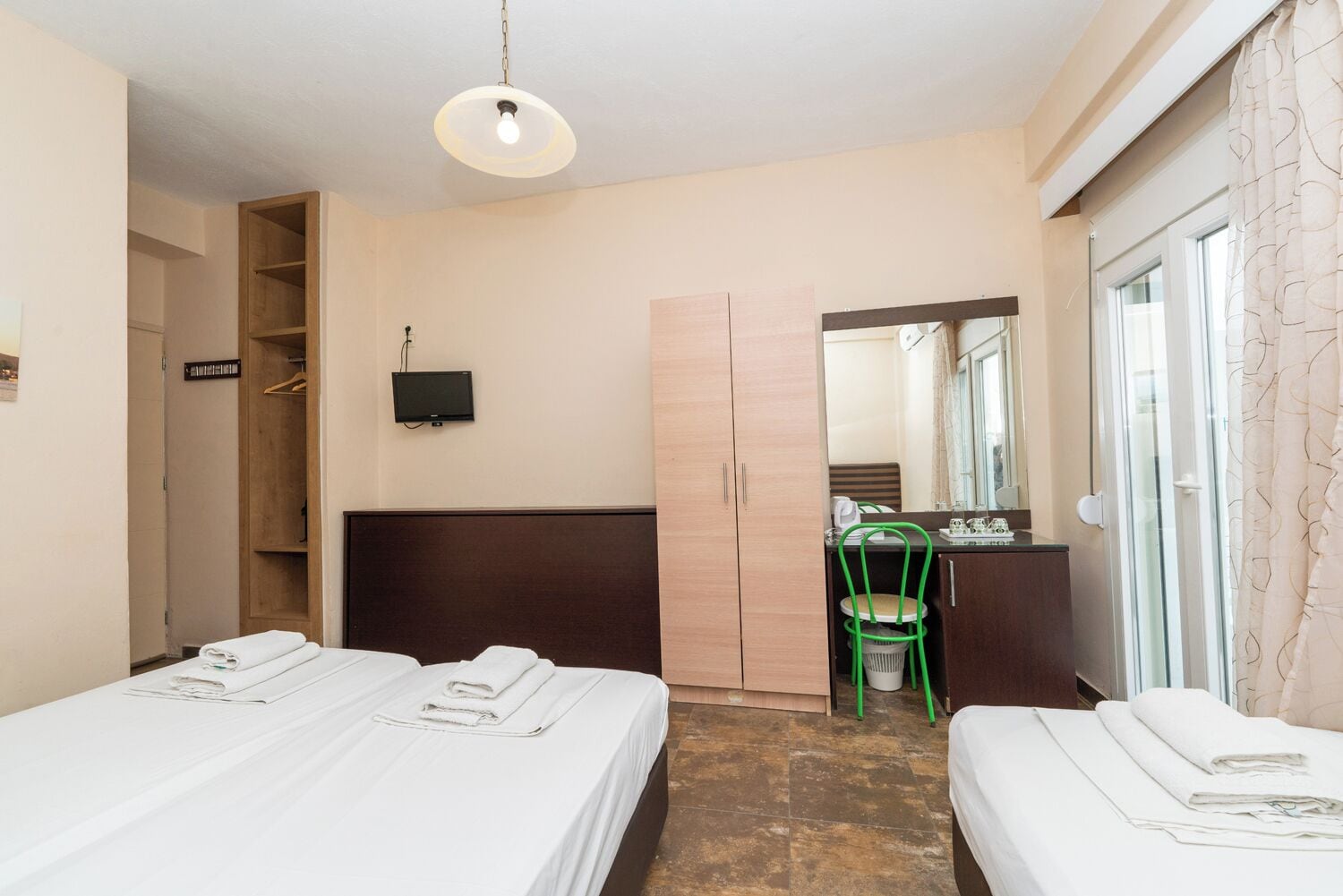 A hotel room with two beds, a desk, a chair, a TV, and a wardrobe.