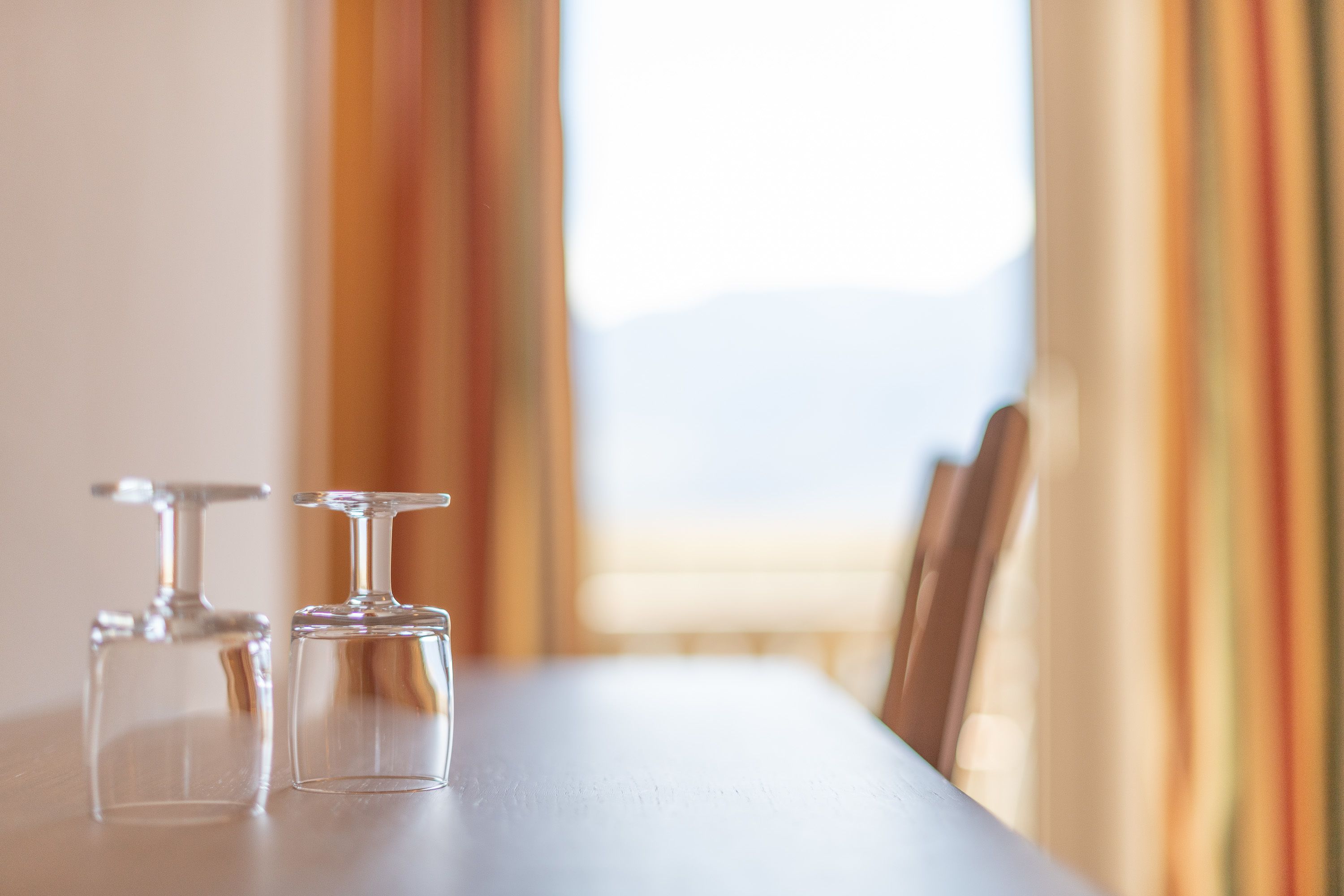 Una mesa de comedor con dos copas de vino vacías y una vista despejada a una ventana con cortinas.