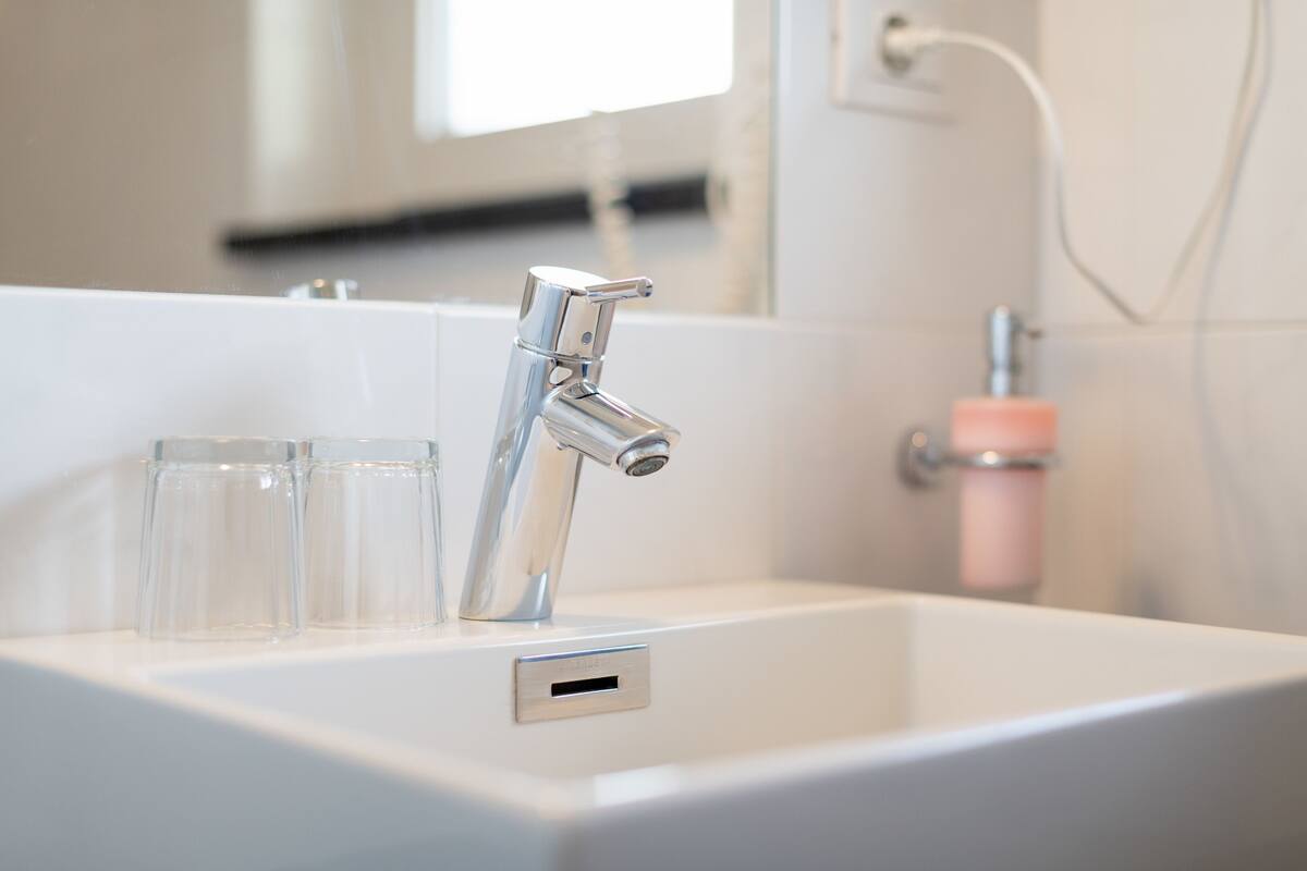 A bathroom sink with a chrome faucet, a mirror, and a soap dispenser.