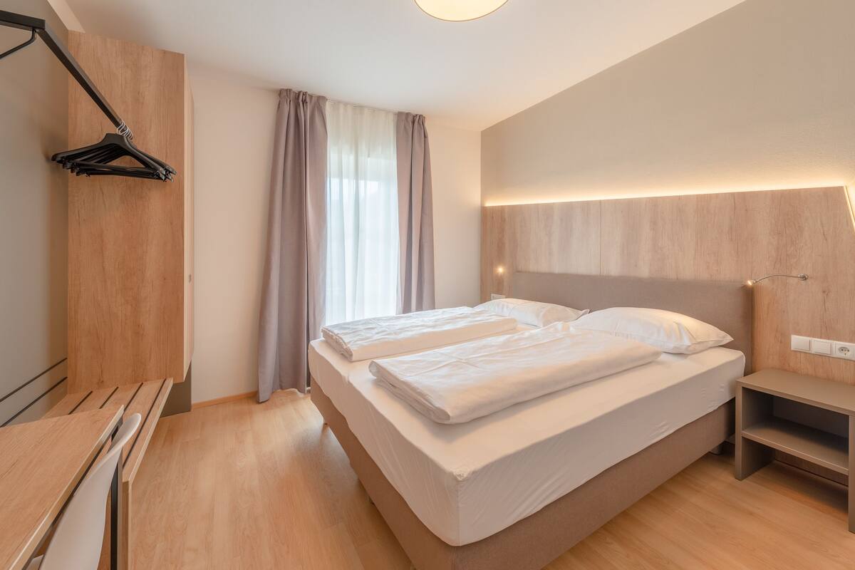 A modern hotel room with two beds, a wooden desk, and a hanging coat rack.