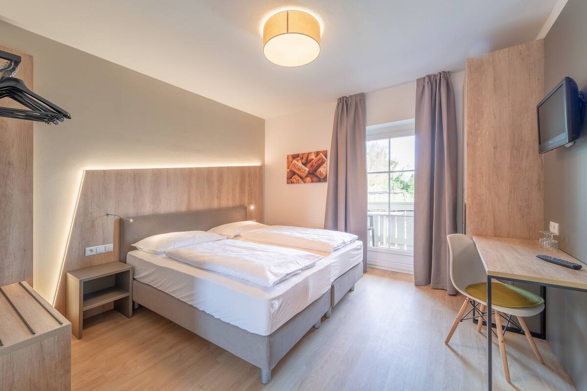 A modern hotel room with a bed, bedside table, desk, chair, and a TV.