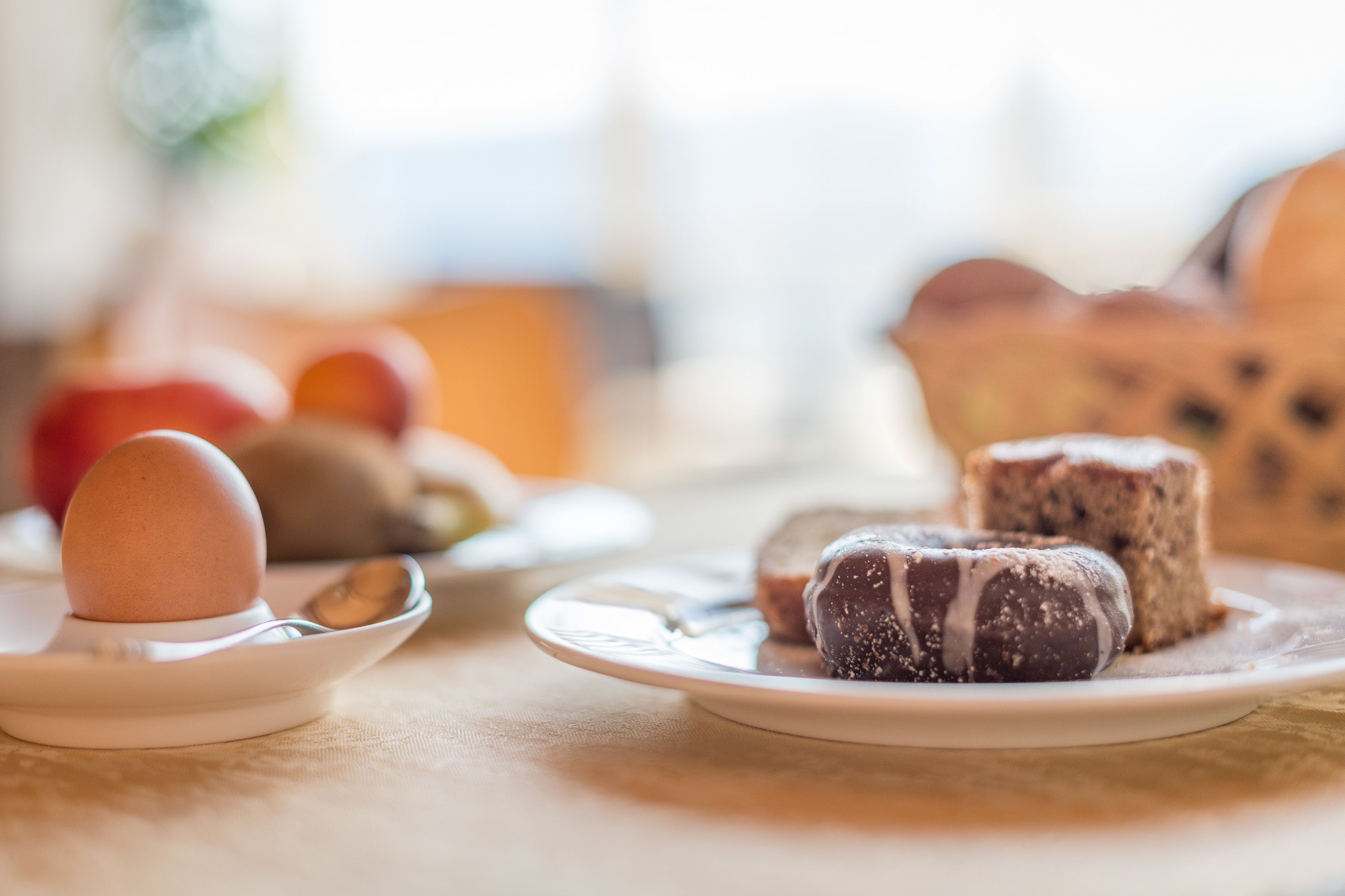 A breakfast setting with a plate of pastries, a boiled egg, and a bowl of fruit.