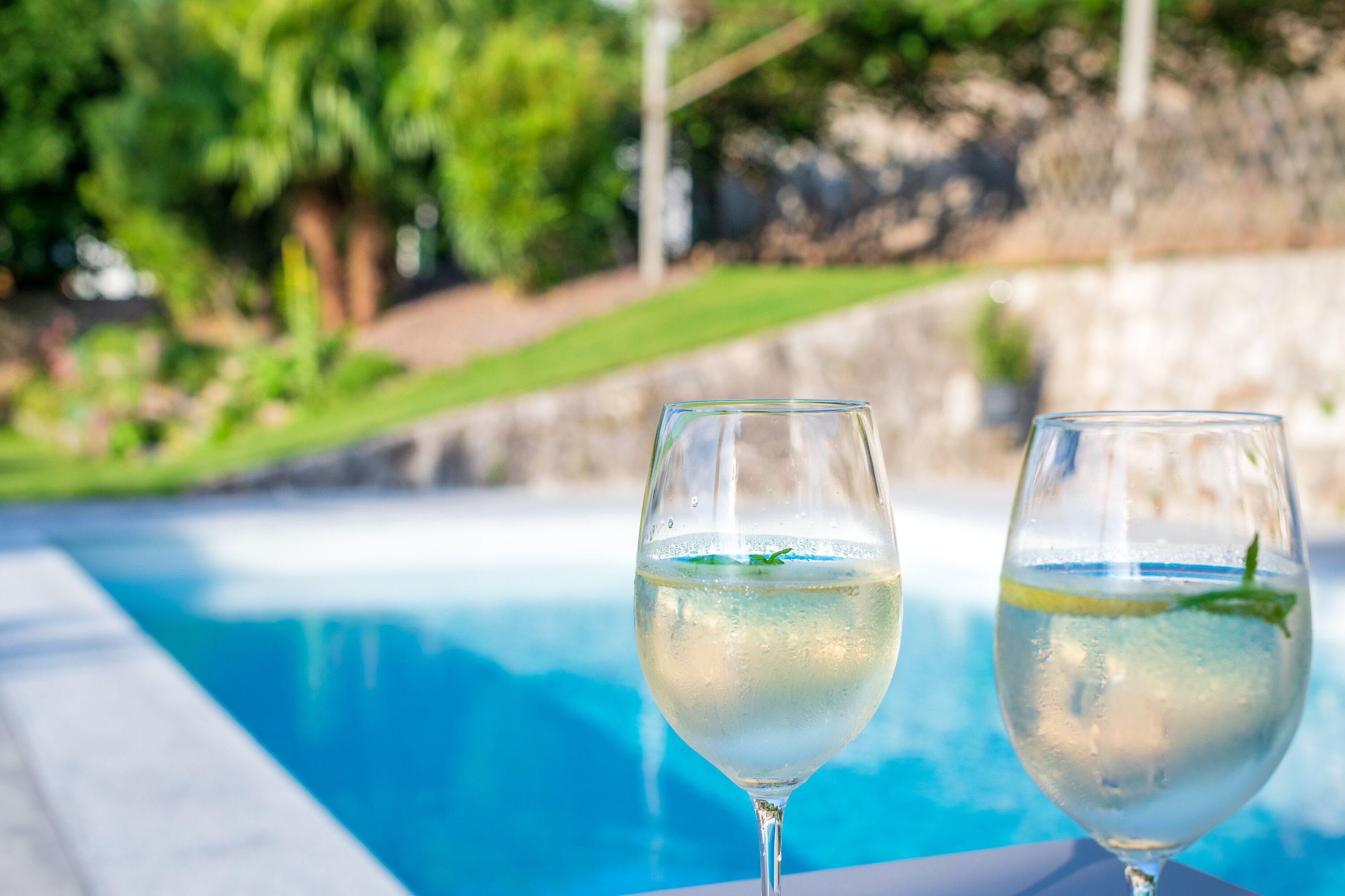 Two glasses of white wine with mint leaves by a poolside.