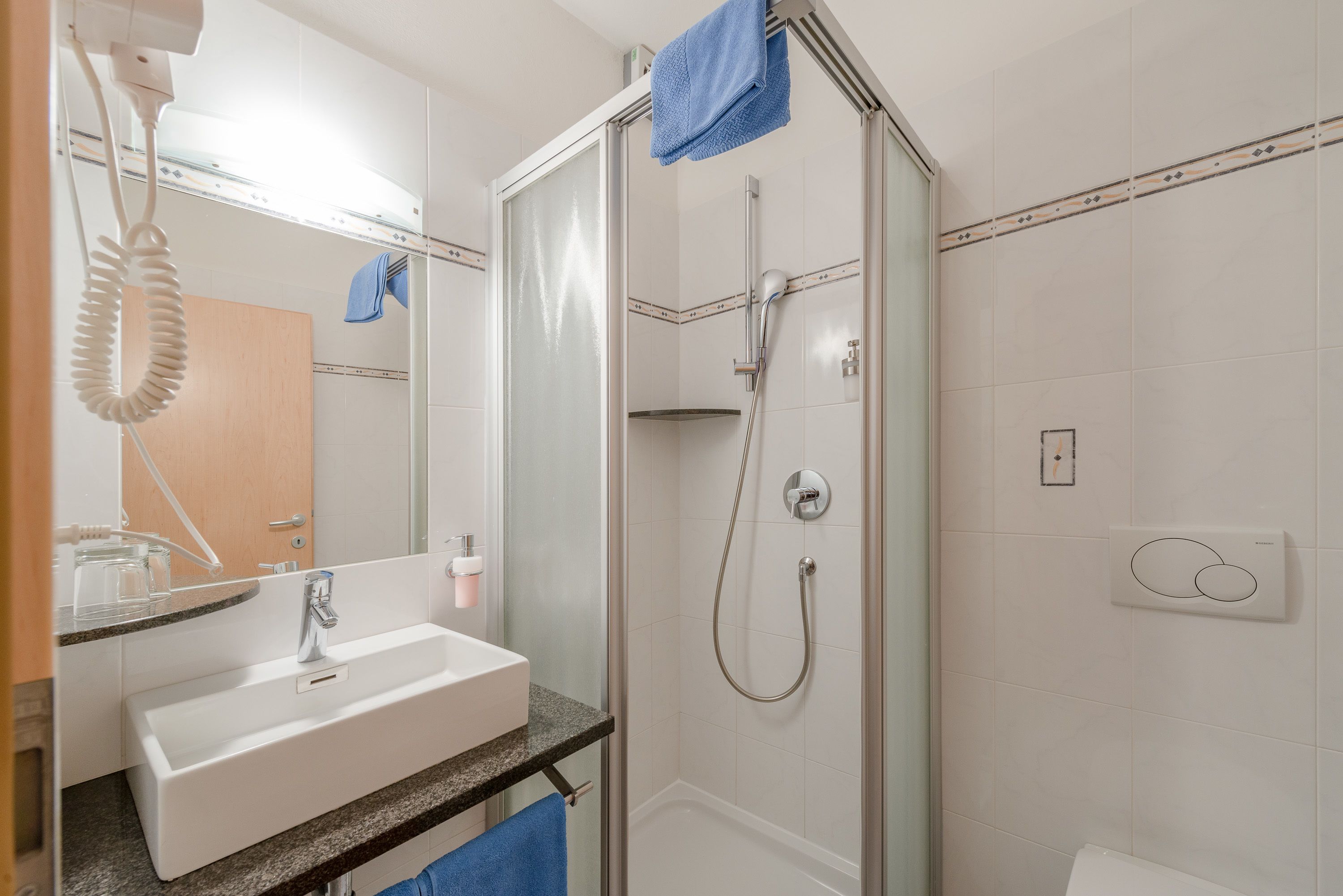 Un baño con ducha de vidrio, lavamanos blanco y un espejo sobre el lavamanos.