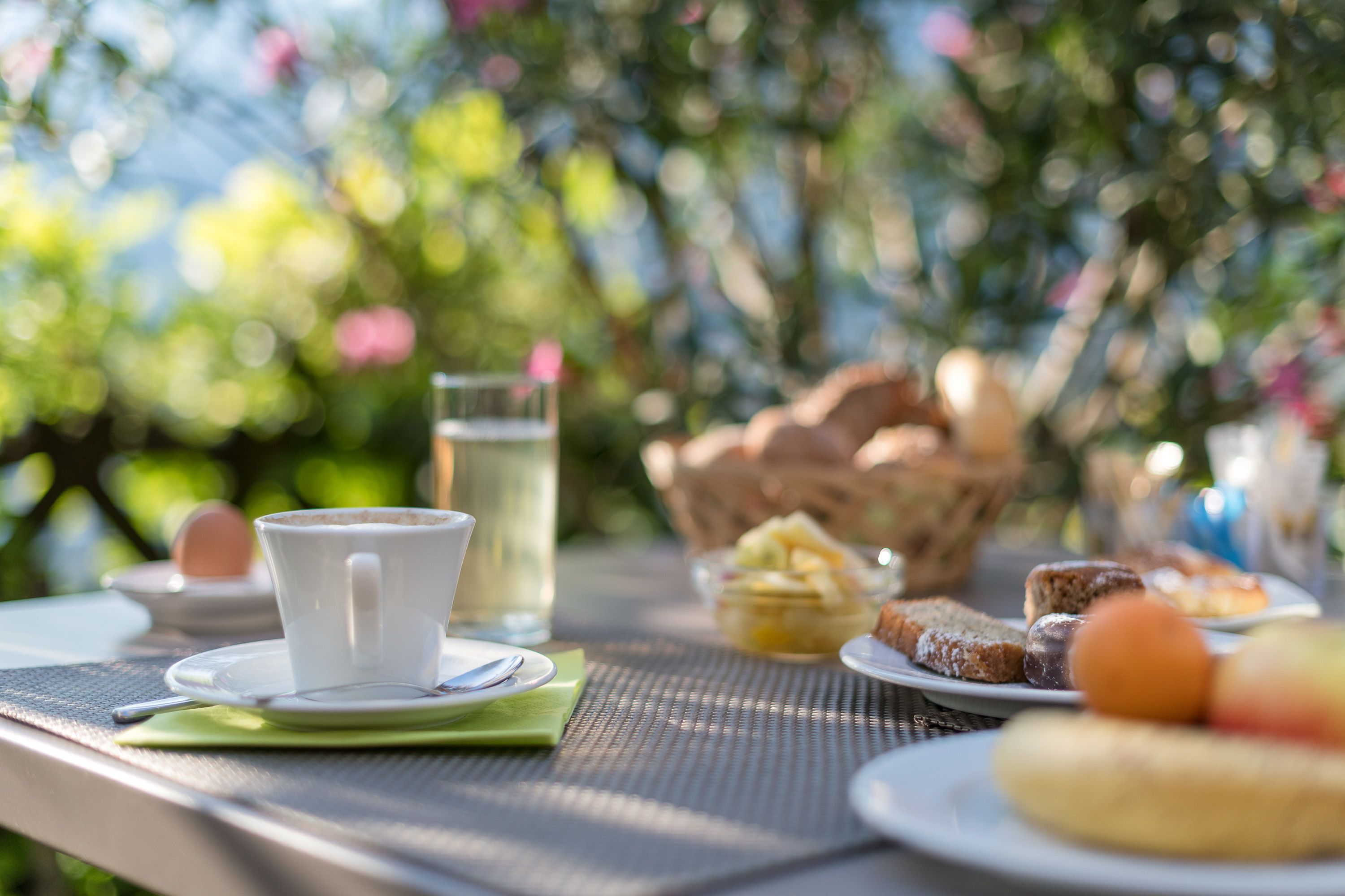 Un tavolo apparecchiato con una tazza, un piattino, un cucchiaino, un bicchiere d'acqua e diversi pasticcini.