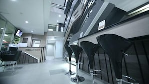 Un área de recepción con diseño moderno, que incluye un mostrador de recepción, taburetes negros y una escalera que sube a un nivel superior.