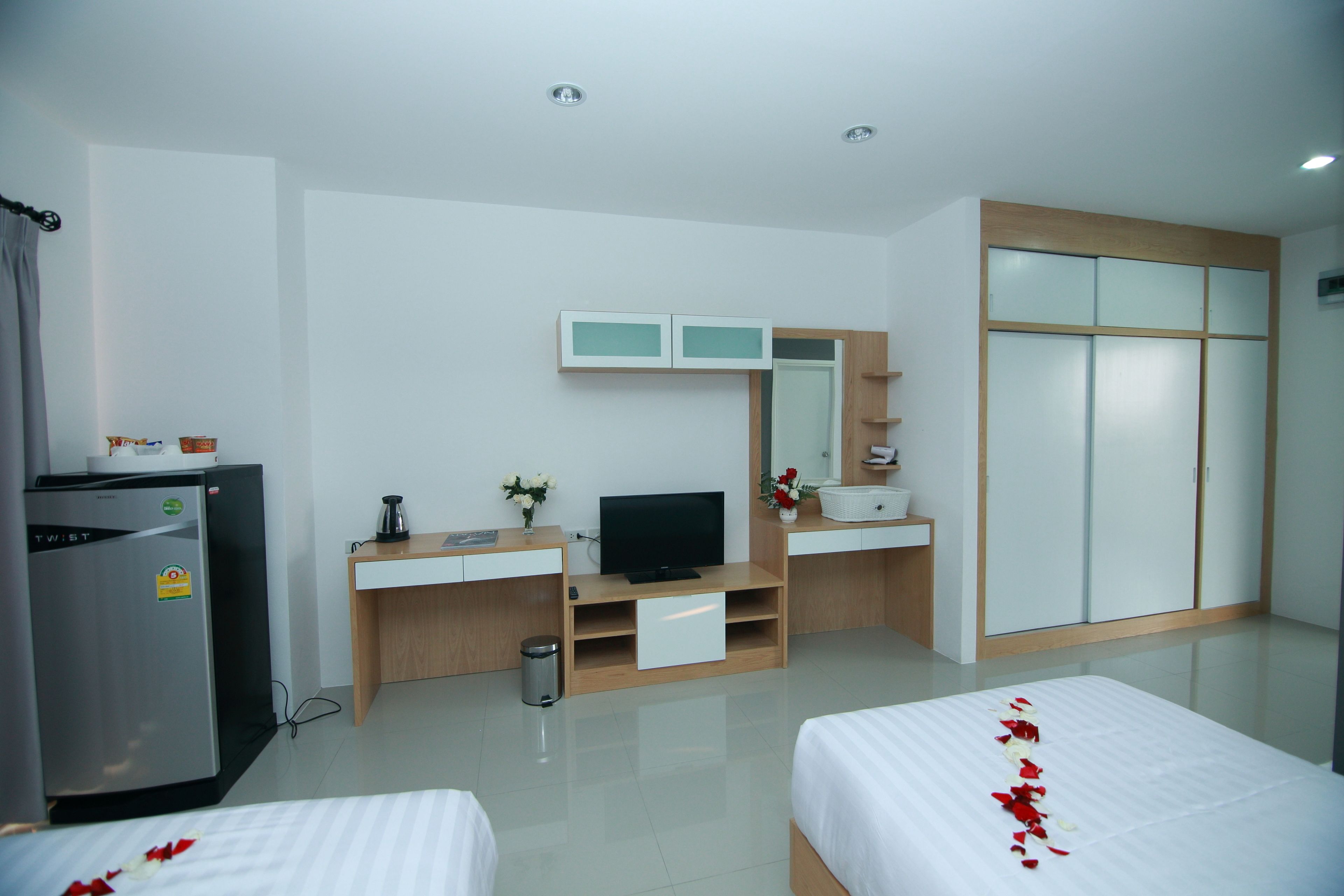 Ein Hotelzimmer mit einem Bett, einem Fernseher, einem Schreibtisch mit Computer, einem Kühlschrank und einem Kleiderschrank.