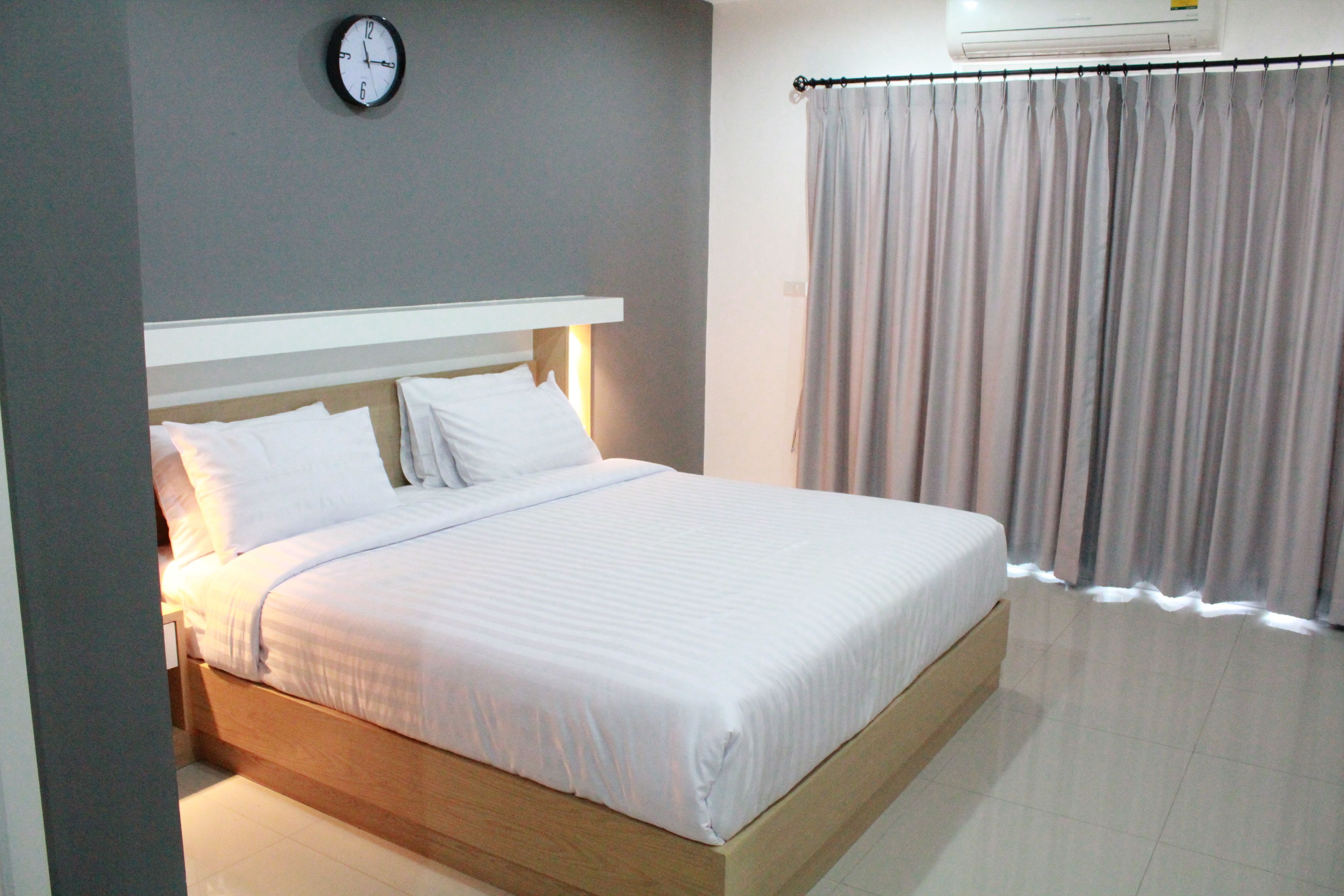 A neatly made bed with white linens in a room with a grey wall and a clock.