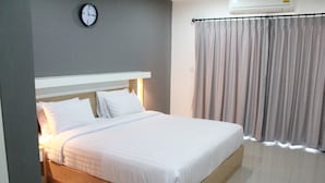 Una cama bien hecha con sábanas blancas en una habitación con pared gris y un reloj.