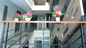 Un moderno vestíbulo de hotel con una escalera de cristal, un mostrador de recepción y dos arreglos florales en la barandilla.