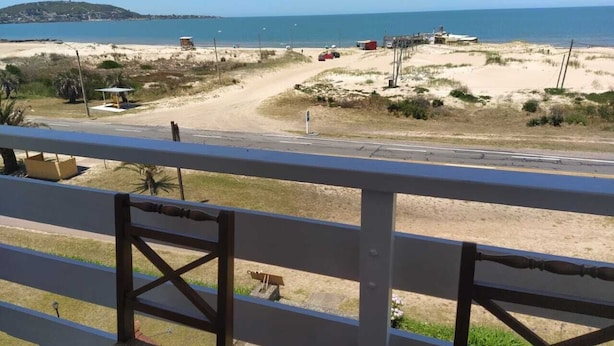 Vista a la playa desde un balcón con barandilla, una playa de arena y el océano al fondo.