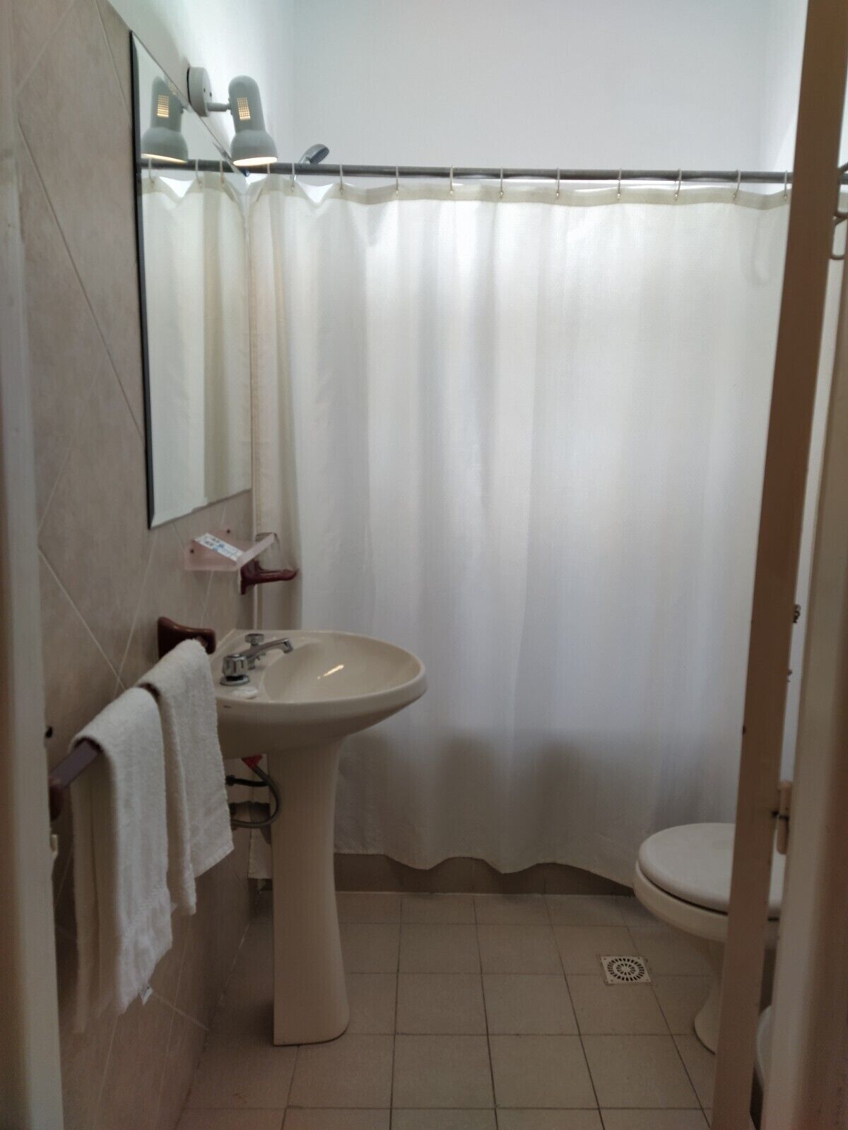 Un baño con lavamanos pedestal, inodoro y cortina de ducha.