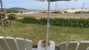 Un patio con sillas y mesa blancas, una bicicleta y vistas a la playa y colinas.