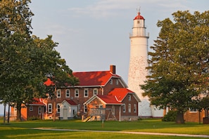 Un phare avec un bâtiment en briques devant, entouré d’arbres.