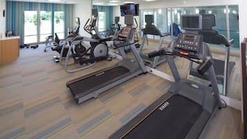 Un gimnasio con cintas de correr, bicicletas estáticas y una zona de pesas.