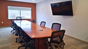A conference room with a long table, six chairs, a flat-screen TV on the wall, and a window with blinds. - Holiday Inn Express & Suites Port Huron by IHG (Port Huron)