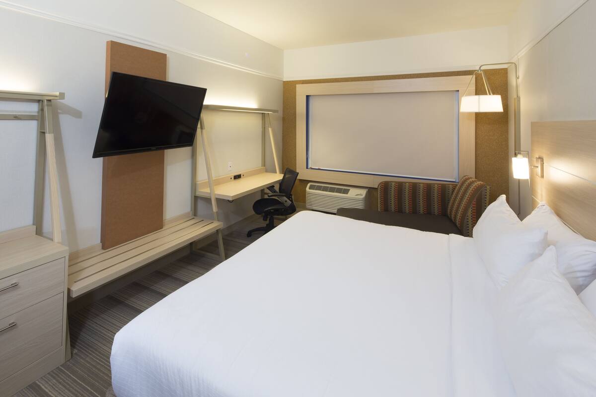 Ein Hotelzimmer mit Bett, Schreibtisch, Stuhl, Fernseher und einem großen Fenster.
