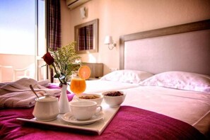 A neatly made bed with a tray of breakfast items including a cup, bowl, and a vase with a flower. - Solimar Dias (Rethymno)