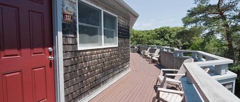 A wooden deck with a red door and a window, surrounded by white railings and outdoor furniture.