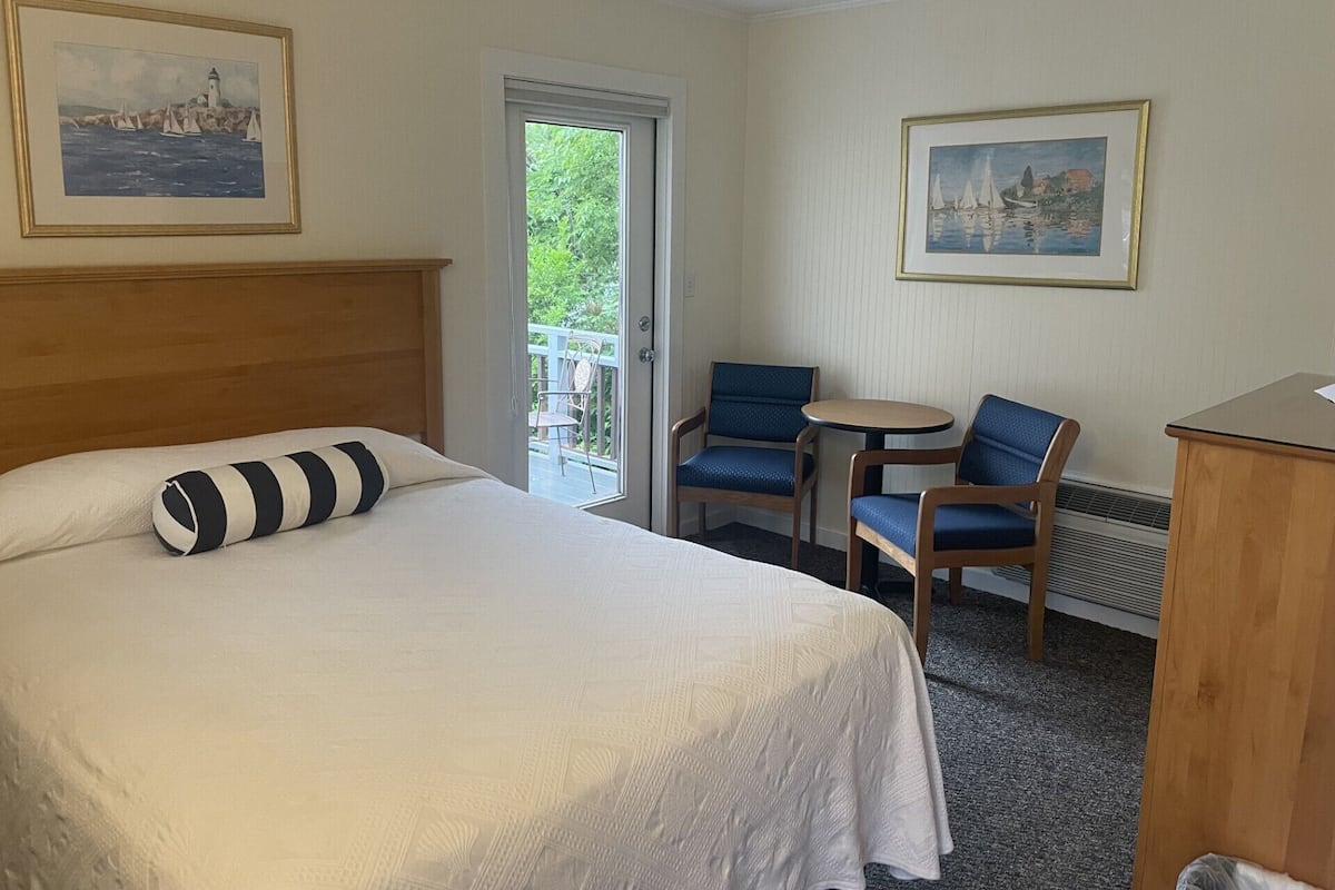 A hotel room with a bed, a desk, two chairs, and two framed pictures on the walls.