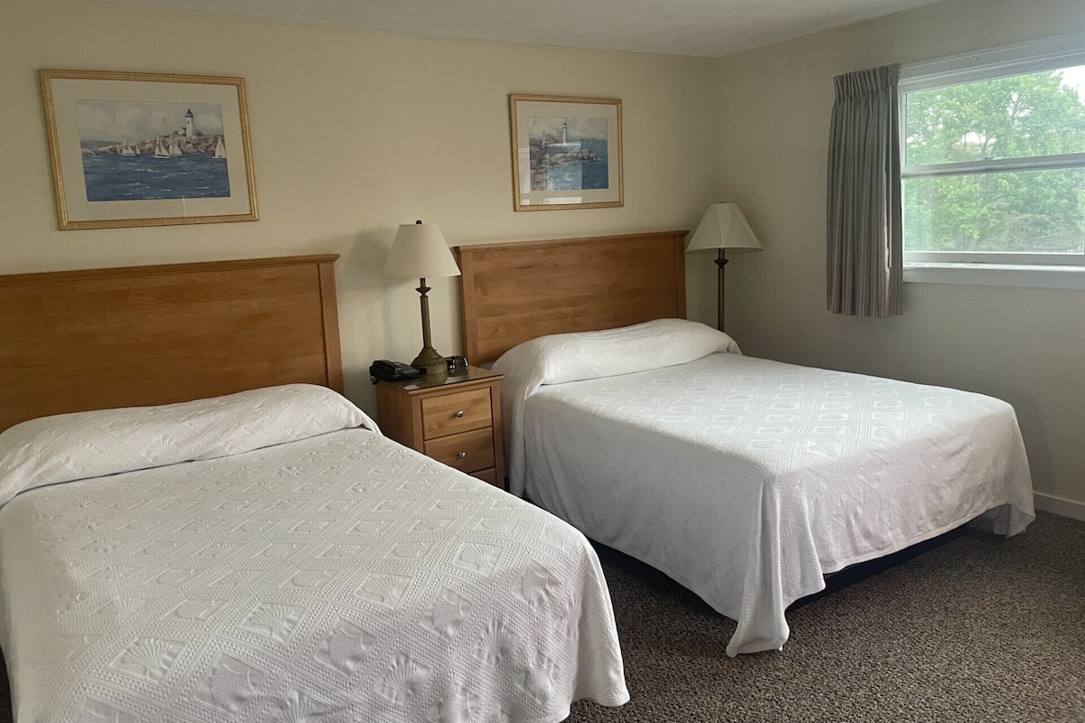 A hotel room with two beds, a nightstand with a lamp, and two framed pictures on the wall.