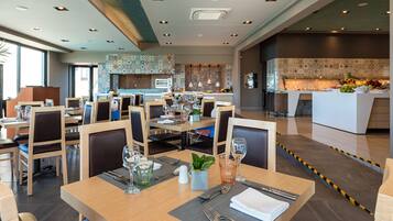 A modern restaurant with wooden tables and chairs, a kitchen area, and a fruit display.