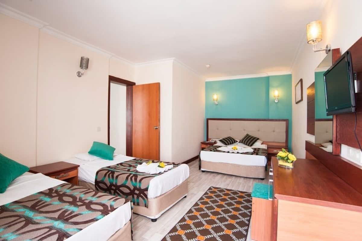A hotel room with two beds, a wooden headboard, a TV, and a small desk.