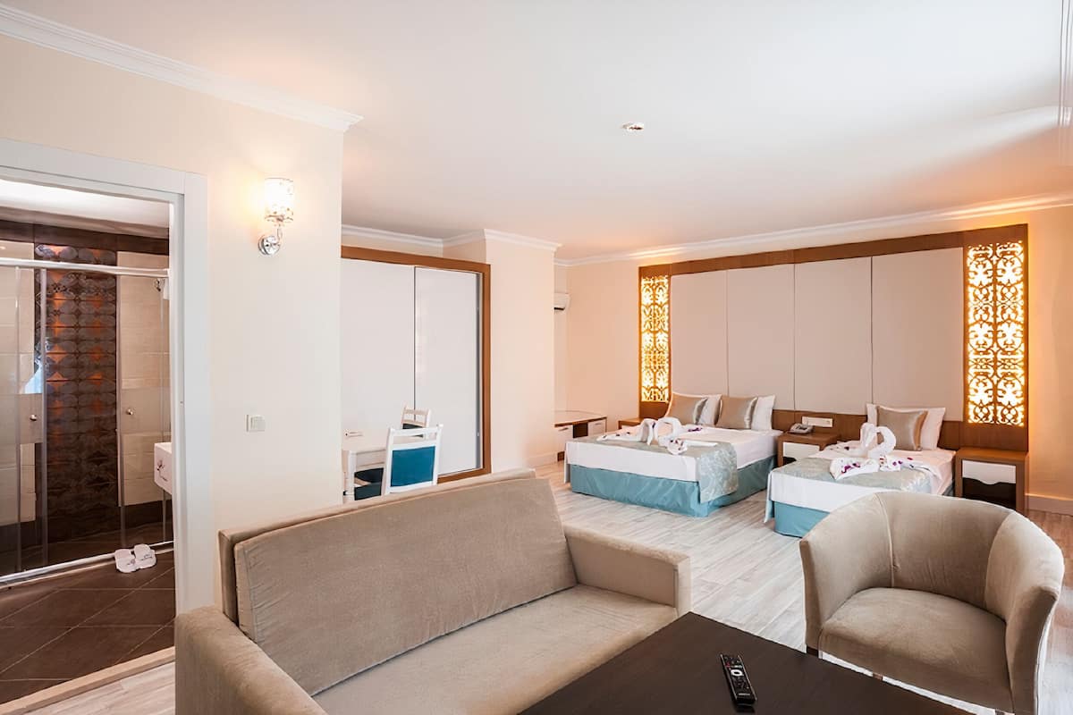 A hotel room with a sofa, two beds, a bathroom with a shower, and a decorative wall panel.
