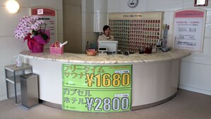 A hotel reception desk with a large sign displaying room rates. - Sauna & Capsule In Okayama (Okayama)