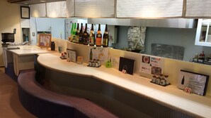 A hotel reception area with a curved counter, various beverage bottles, informational signs, and a phone. - Sauna & Capsule In Okayama (Okayama)