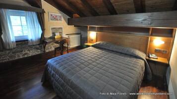 Ein gemütliches Schlafzimmer mit einem großen Bett, Holzbalken, einer Steinwand und einem kleinen Schreibtisch mit Stuhl.
