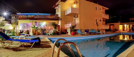 Un área junto a la piscina con sillones de descanso y un edificio con un letrero que dice "CHILL OUT".
