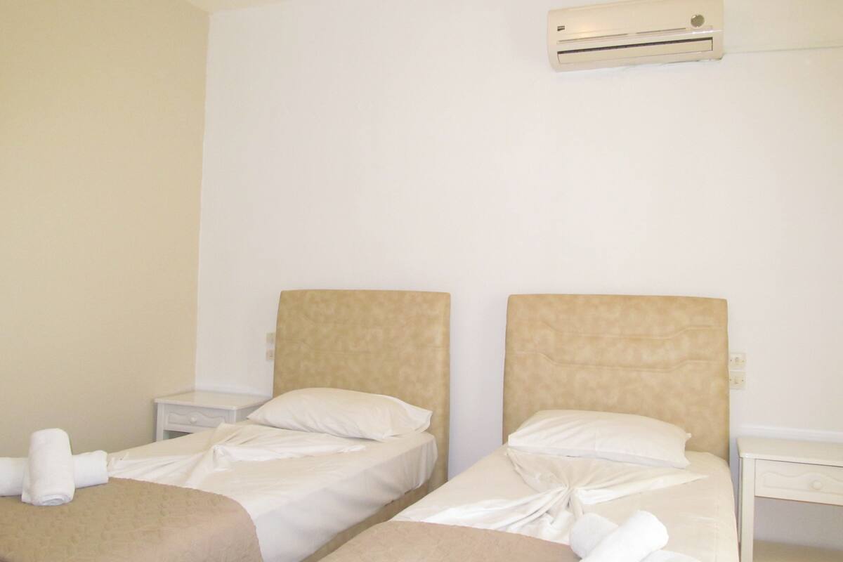 Una habitación de hotel con dos camas, una mesita de noche y un aire acondicionado en la pared.