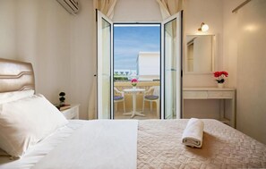 A hotel room with a bed, a bedside table, a small table with chairs, a balcony, and a bathroom with a mirror and a sink. - Irini Studios (Hersonissos)