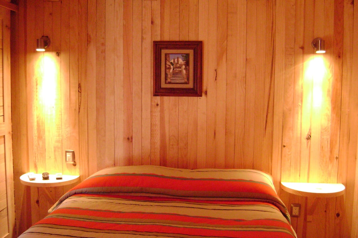 A wooden-paneled room with a bed, two bedside lamps, and a framed picture on the wall.