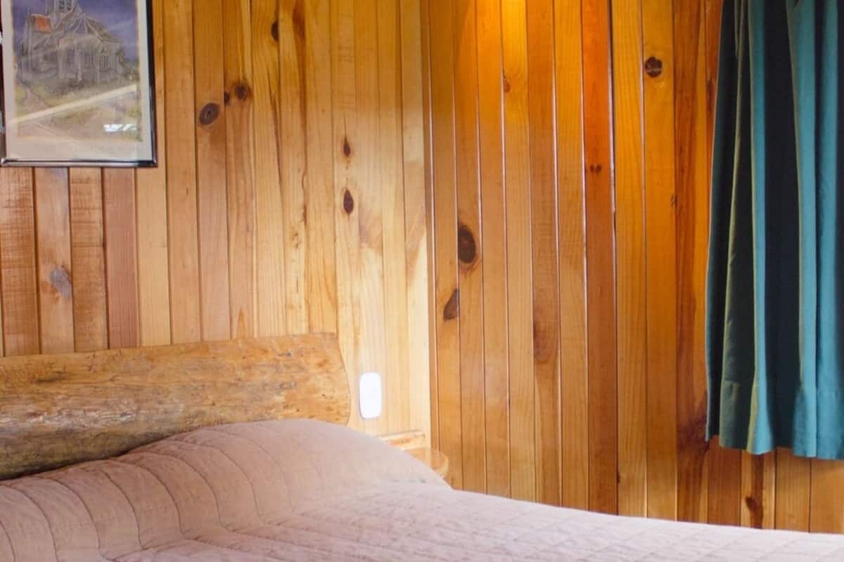 A wooden-paneled room with a bed, a framed picture on the wall, and a curtain.