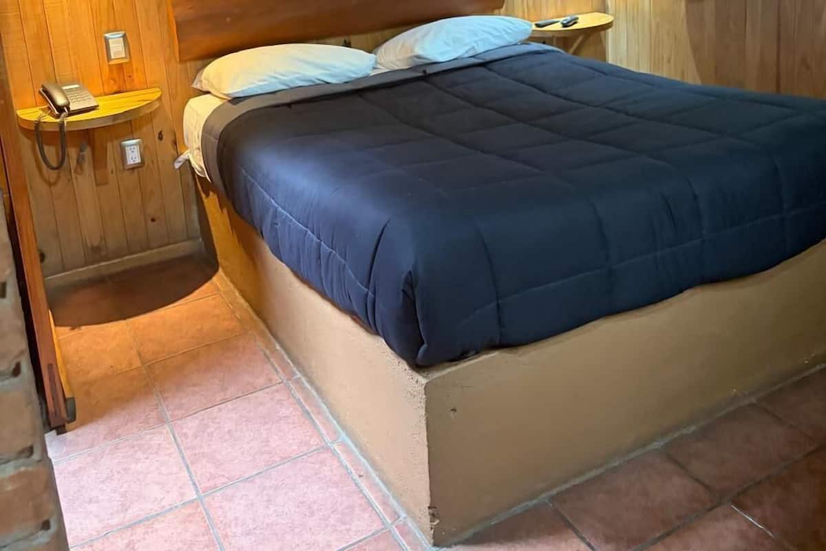 A wooden-paneled room with a bed, bedside tables, a telephone, and a window with curtains.