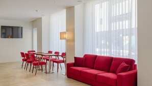 A modern living room with a red sofa, a dining table with chairs, and large windows with sheer curtains. - Porto Downtown (Porto)