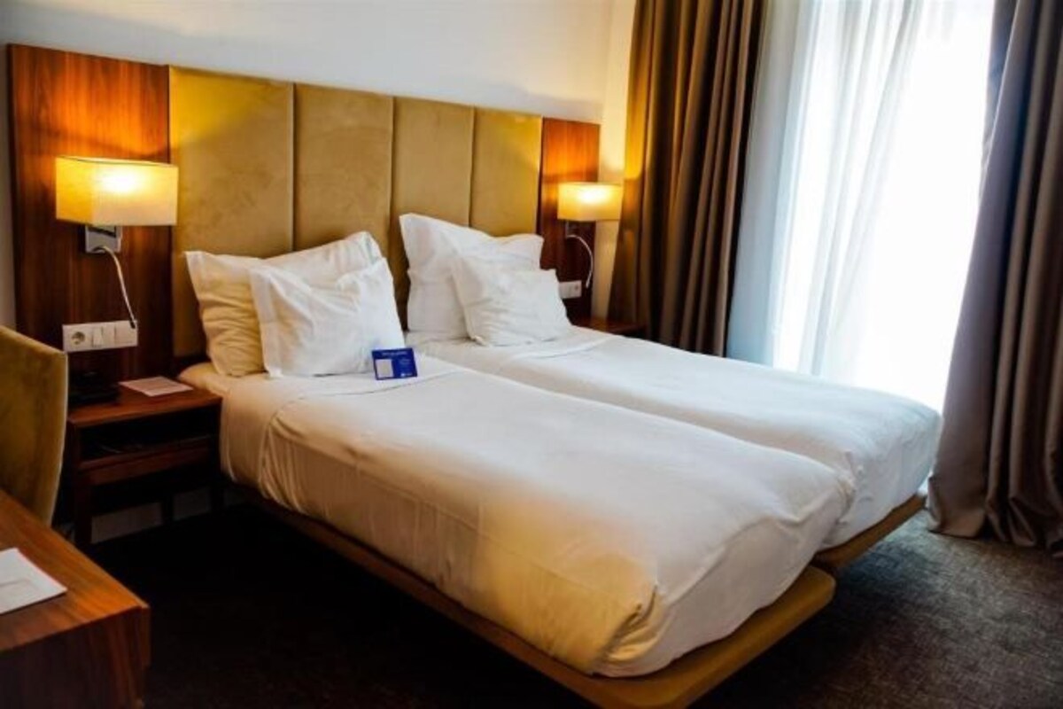 A double bed with white linens, two bedside tables, and lamps.