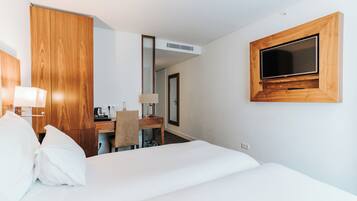 A hotel room with a bed, a desk, a chair, a TV mounted on the wall, and a mirror.