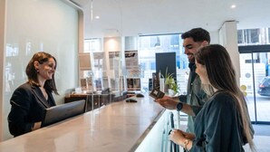 A reception area with a receptionist, a guest holding a passport, and a counter with a laptop. - Porto Downtown (Porto)